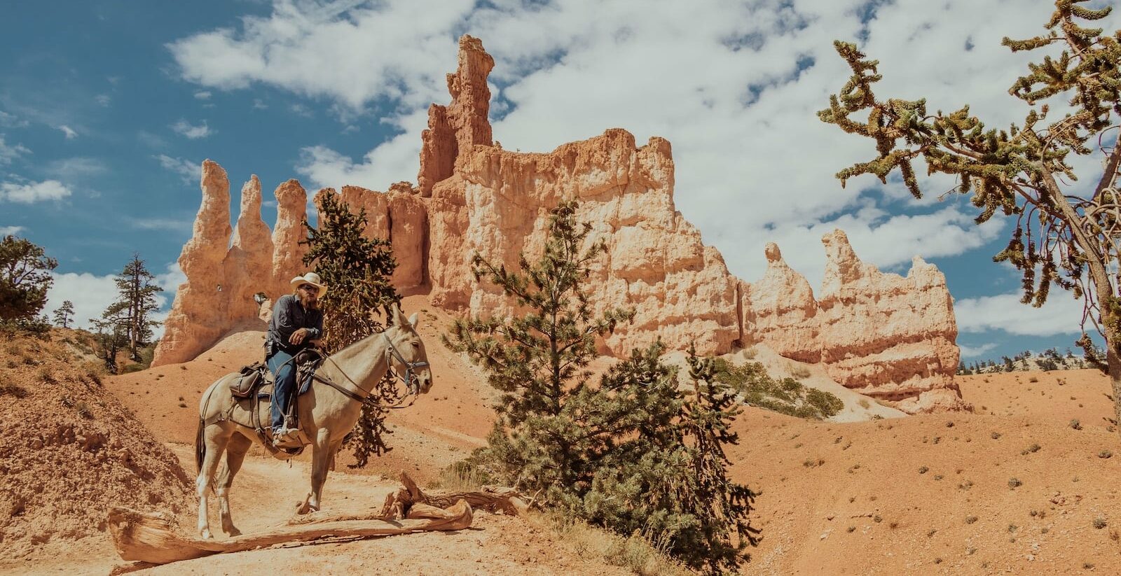 man riding horse on brown rock formation under blue sky and white clouds during daytime